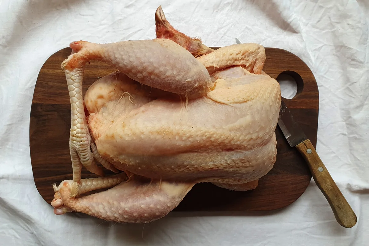 Poulet entier nettoyé, prêt à cuire, posé sur une planche en bois
